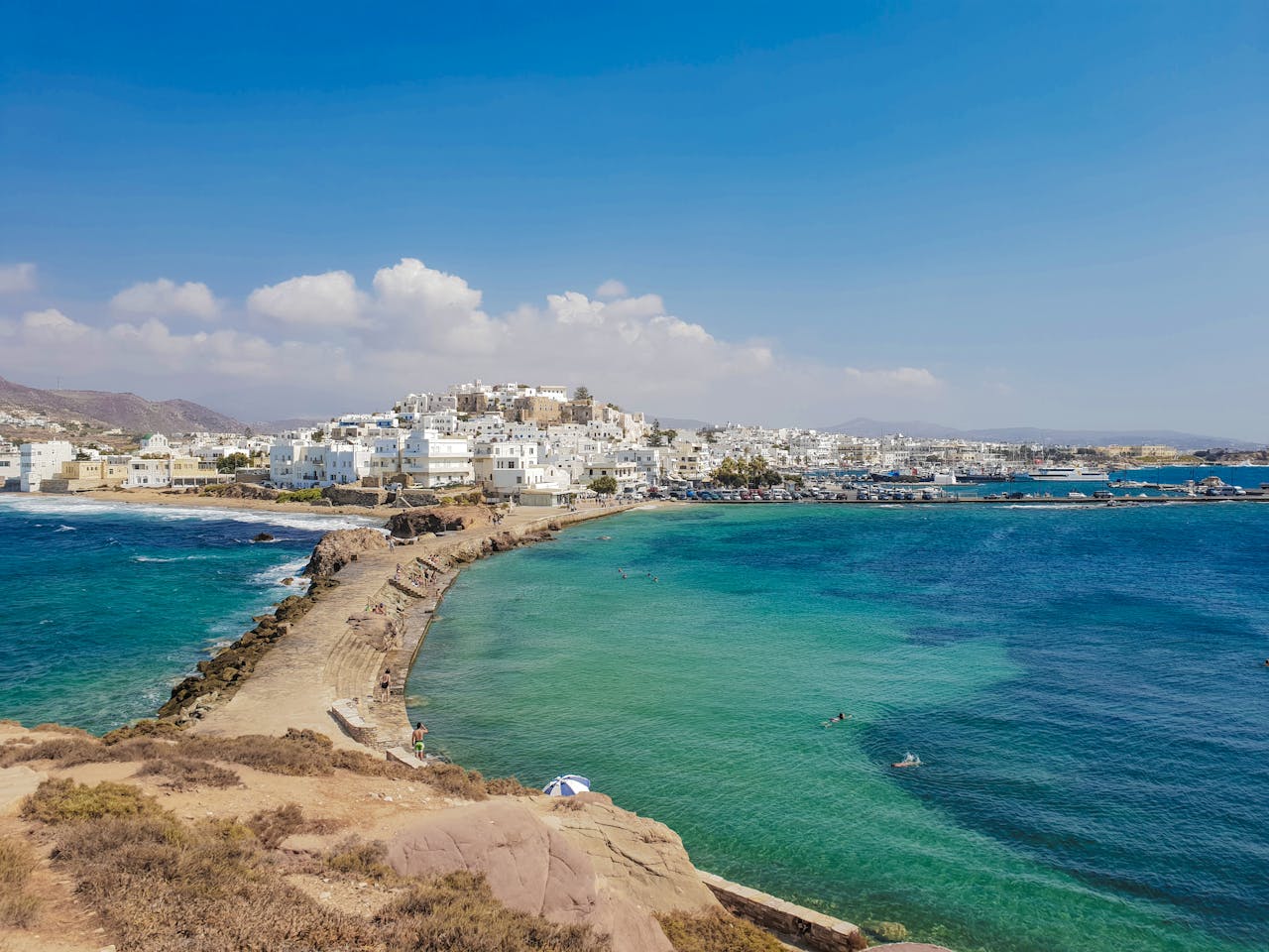 hero-gallery-01 Captivating coastal view of Naxos Town with bright blue waters under a clear summer sky.